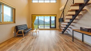 A spacious living room with a black leather sofa, a small round table, and a staircase with wooden steps. - Gyeongpoen Pension (Gangneung)