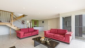 Ein geräumiger Wohnbereich mit zwei roten Sofas, einem schwarzen Couchtisch und einer Treppe, die zu einer oberen Ebene führt.