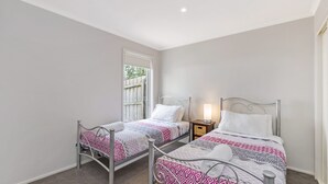 Ein Schlafzimmer mit zwei Betten mit Metallgestell, jeweils mit gemusterten Bettbezügen und einem Nachttisch mit Lampe.
