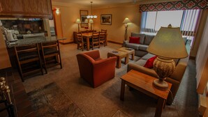 Una sala de estar con sofá, sillón, mesa de centro y lámpara. Hay un comedor con mesa y sillas.