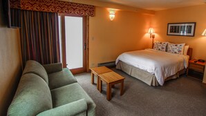 Habitación de hotel con sofá verde, una mesa de madera, cama con ropa blanca y mesita de noche con lámpara.