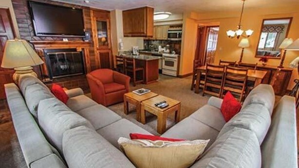 Una sala de estar con un sofá grande de color gris, un sillón rojo, una mesa de centro de madera y un televisor.