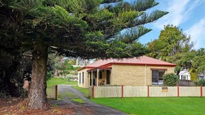 Un bâtiment en pierre de deux étages, avec un toit rouge, une cour clôturée et un grand arbre au premier plan.