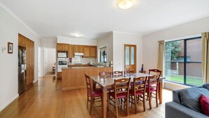 Une cuisine spacieuse avec des meubles de rangement en bois, une table à manger avec des chaises et une grande fenêtre donnant sur l’extérieur.