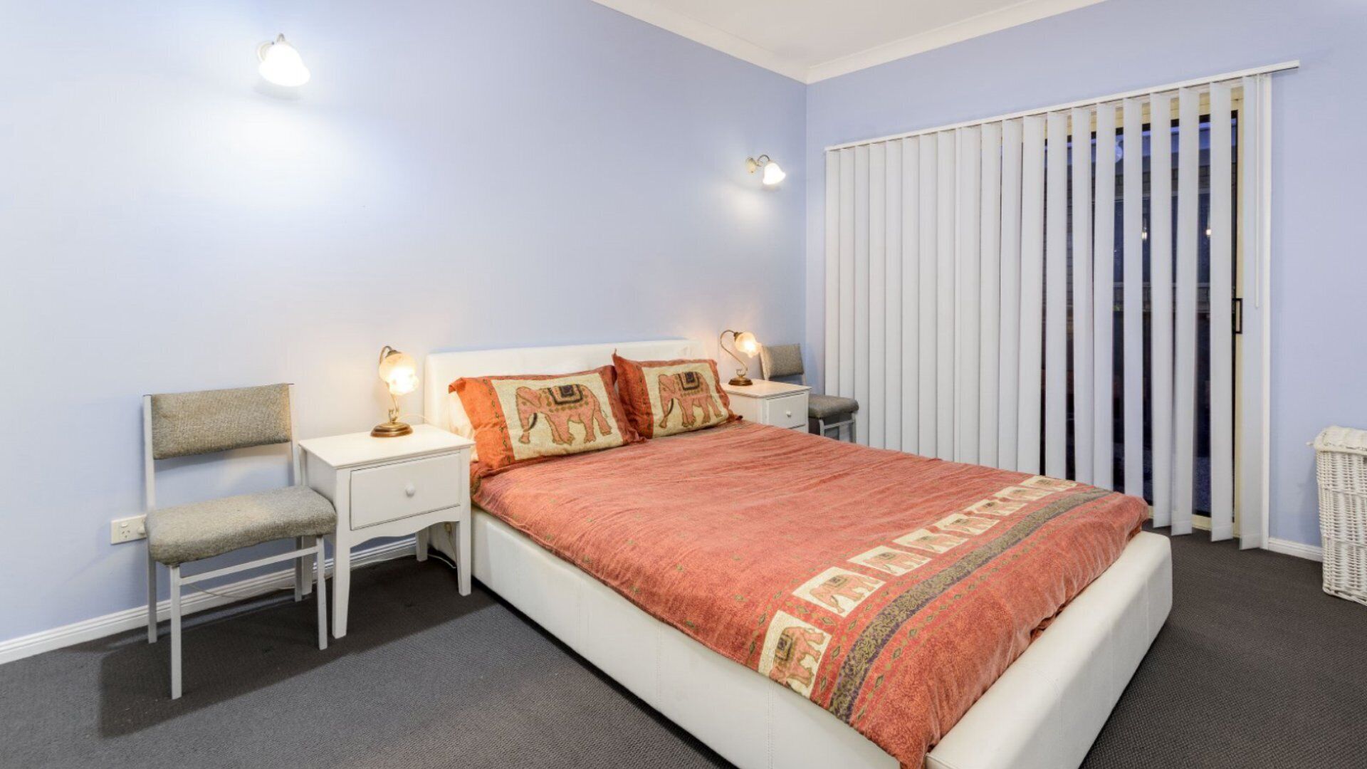 A bedroom with a bed, two bedside tables with lamps, a chair, and a window with blinds.