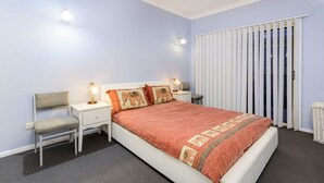 Een slaapkamer met een bed, twee nachtkastjes met lampen, een stoel en een raam met jaloezieën.