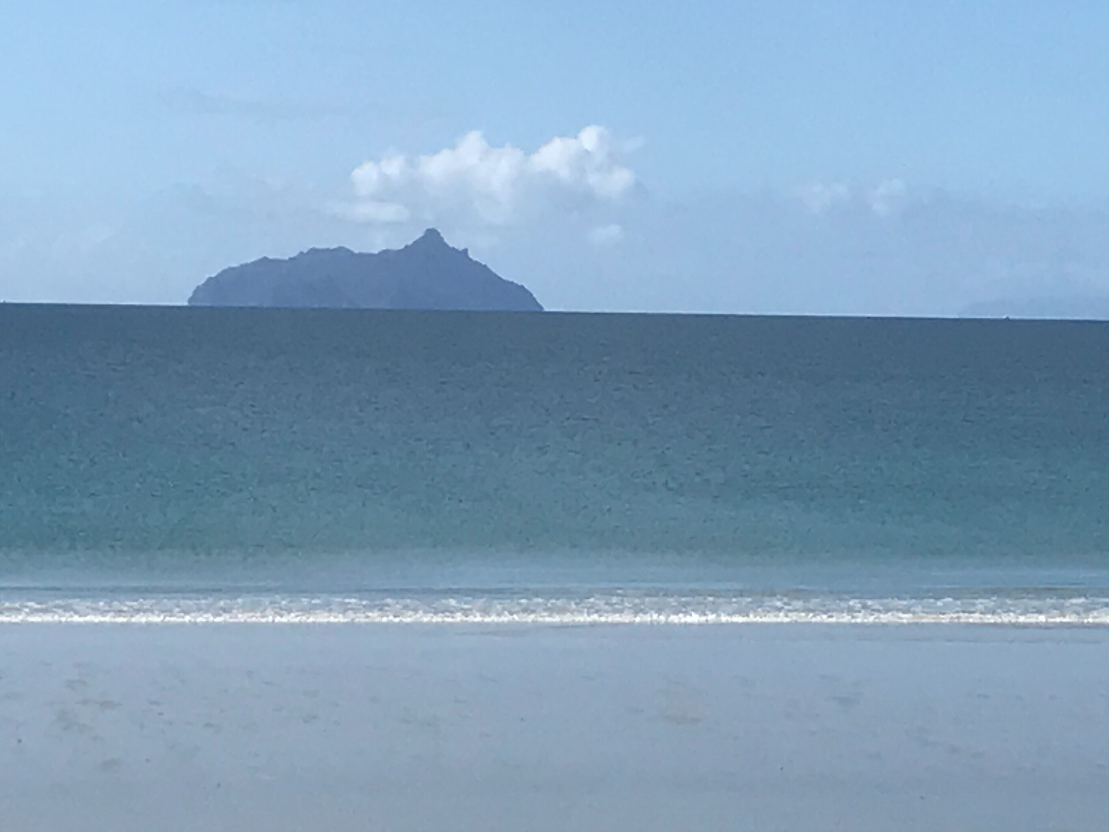 A beach with a calm sea and a distant mountain.