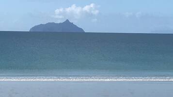 A beach with a calm sea and a distant mountain.