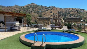 A swimming pool with a wooden deck, lounge chairs, and a pergola with a thatched roof. - Beautiful rural house with swimming pool and sea views, special discounts (Algarrobo)