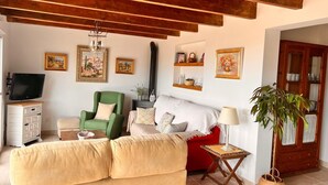 A cozy living room with a sofa, armchair, and TV, wooden beams on the ceiling, and artwork on the walls. - Beautiful rural house with swimming pool and sea views, special discounts (Algarrobo)