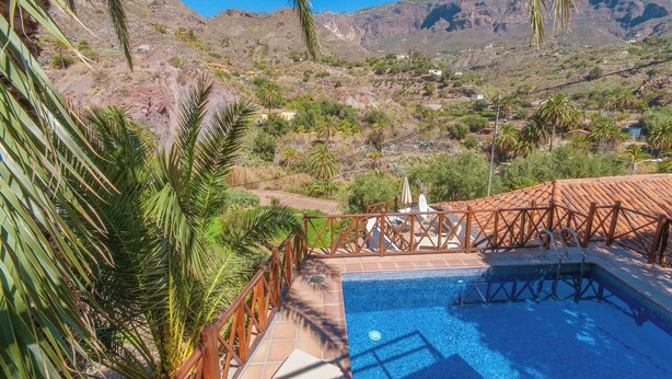 Un área de piscina con cubierta de madera y vistas a un paisaje montañoso.