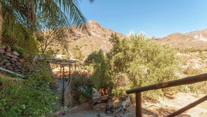 Un espacio rústico al aire libre con pared de piedra, estructura de madera y vegetación natural.