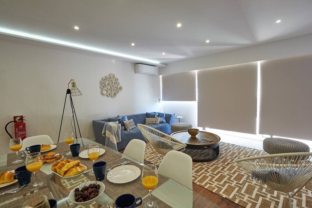 A modern living room with a dining area, featuring a sofa, chairs, a coffee table, and a dining table set with food and drinks.
