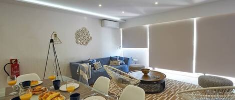 A modern living room with a dining area, featuring a sofa, chairs, a coffee table, and a dining table set with food and drinks.
