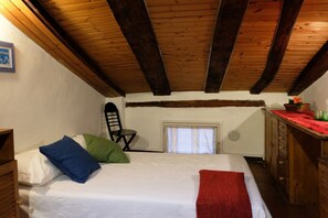 A bedroom with a wooden ceiling, a bed with pillows, a chair, a window, and a dresser.
