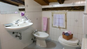 A bathroom with a sink, bidet, and toilet, wooden ceiling beams, and a tiled wall.