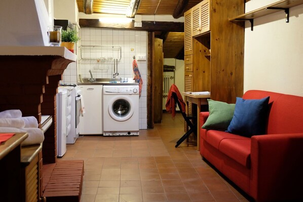 A compact kitchen with a washing machine, a red sofa, and a small table with a red cloth.