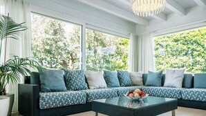 Una sala de estar moderna con un sofá modular, una mesa de centro de cristal y grandes ventanas con vistas a la vegetación.
