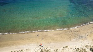 Vista aérea de una playa con agua turquesa cristalina, una orilla de arena y algunos objetos dispersos.
