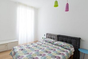 A bedroom with a bed, a window with curtains, and two hanging lamps. - GuestHost - Beautiful and spacious 76 sqm apartment located in a strategic position just a short distance from Piazza Oberdan, Porto Vecchio, Palazzo Gopcevich and Piazza Unita d'Italia. The particular position of the house allows to reach easily the his (Trieste)