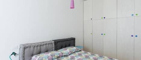 A bedroom with a bed, a wardrobe, and a desk with a lamp.