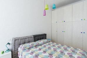 A bedroom with a bed, a wardrobe, and a desk with a lamp.