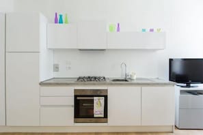 A modern kitchen with white cabinets, a gas stove, an oven, and a television.