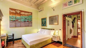A bedroom with a large bed, a wooden floor, a desk with a chair, and a painting on the wall.