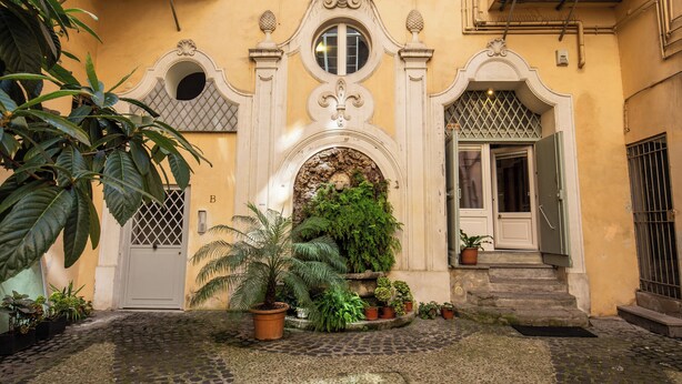 A courtyard with a cobblestone path, a central fountain, and potted plants.