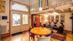 A spacious living area with a wooden dining table, a brown sofa, and a large window overlooking a street.