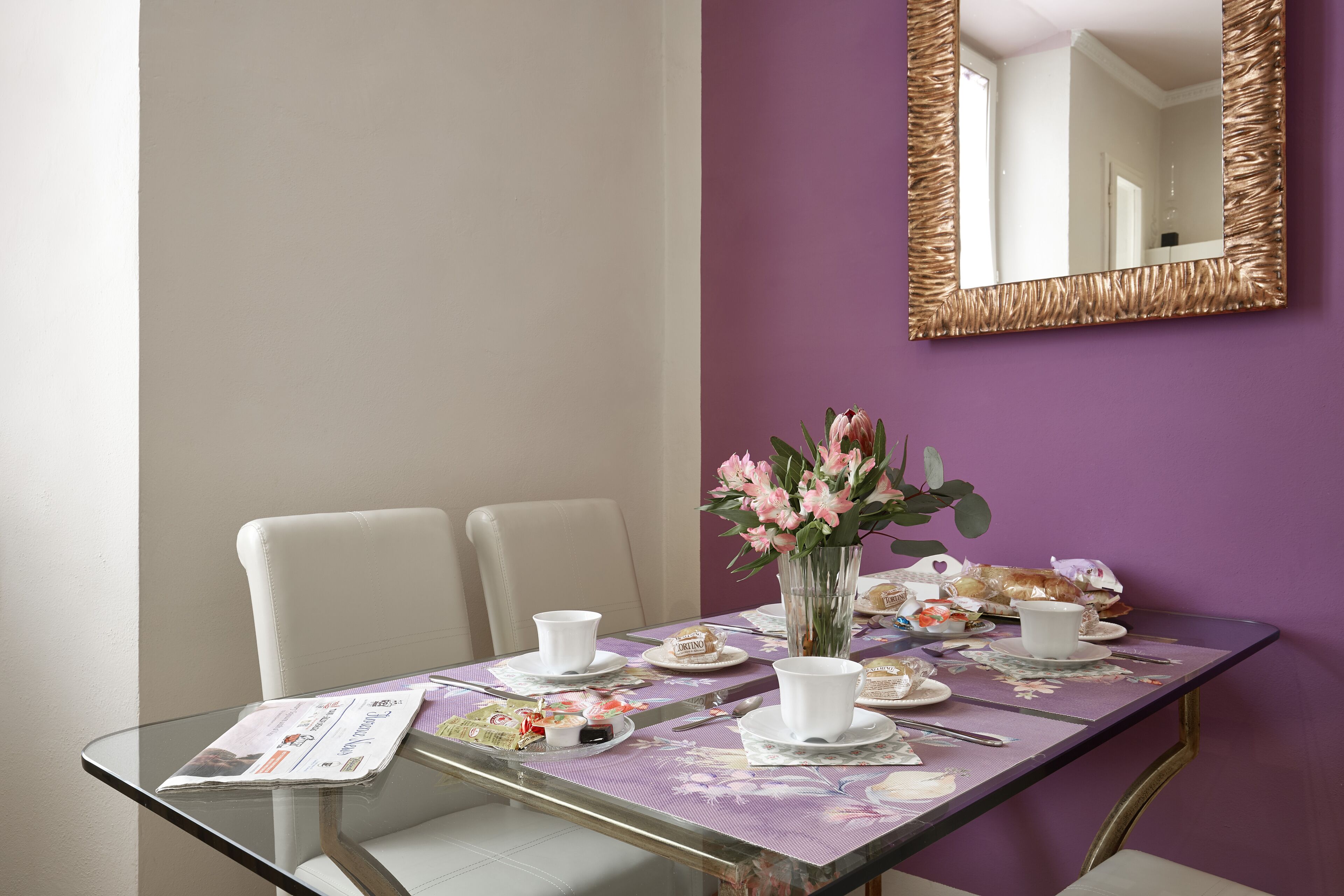 A dining table set with white cups, saucers, and a vase of pink flowers.