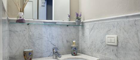 Un baño con lavamanos de mármol, tocador de madera y un espejo con iluminación.