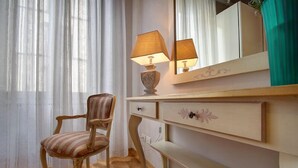 A room with a wooden chair, a vanity with a mirror, a lamp, and a shelf with books. - The elegance in the heart of Florence (Firenze)