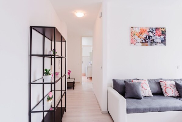 A modern living room with a grey sofa, a black metal shelving unit with plants, and a colorful abstract painting on the wall.
