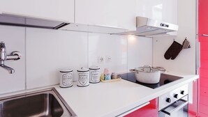 Moderni keittiö, jossa on valkoiset kaapit, ruostumattomasta teräksestä valmistettu allas, liesi ja liesituuletin.