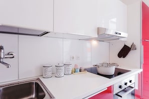 Una cucina moderna con mobili bianchi, un lavello in acciaio inossidabile, un fornello e una cappa aspirante.