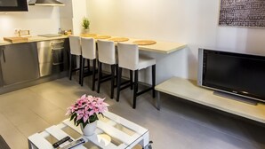 Een moderne keuken met een eethoek, roestvrijstalen apparatuur, een flatscreen televisie en een plant in pot.