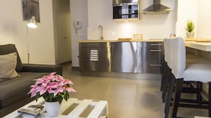 Een moderne keuken met roestvrijstalen apparatuur, een eethoek met tafel en stoelen, en een woonkamer met een bank en een potplant.