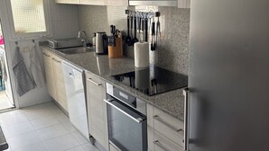 A modern kitchen with light wood cabinets, a stainless steel refrigerator, a built-in oven, and a granite countertop.