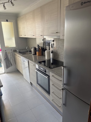 Cozinha moderna com armários de madeira clara, geladeira de aço inoxidável, forno embutido e bancada de granito.