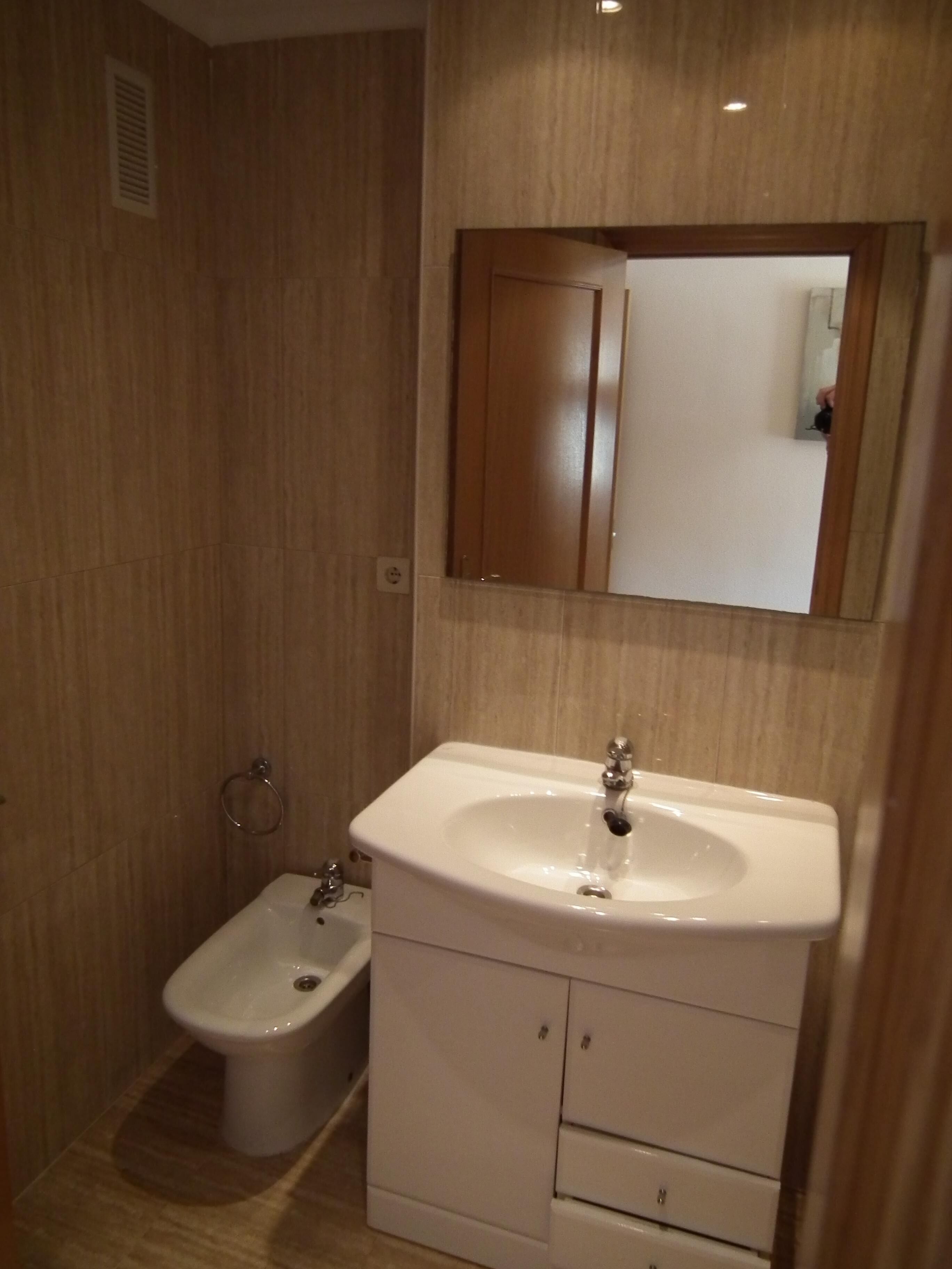 Et badeværelse med en hvid vask, et spejl over vasken og et bidet til venstre.