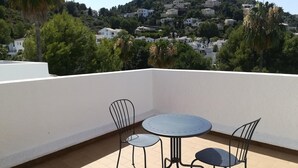 Una terrazza con un tavolo rotondo e sedie, un muro bianco e vista su una collina con edifici.