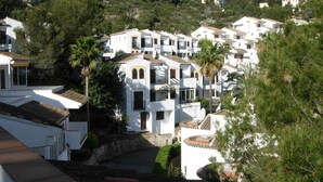 Una zona residenziale su una collina, con edifici bianchi, alcuni con balconi, circondata da vegetazione.