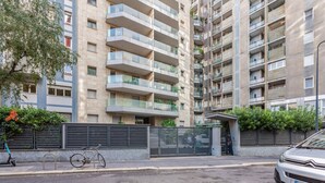 Un edificio residencial de varios pisos con balcones, un acceso con reja y un coche estacionado.