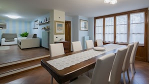 A dining area with a wooden table, white chairs, and a lace table runner. There is a sofa and a plant in the adjacent living area. - Two-storey villa with large private pool and beautiful landscaped garden (Castiglion Fiorentino)