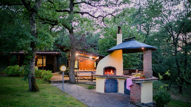 A brick outdoor kitchen with a chimney, surrounded by trees and a well-maintained lawn. - Two-storey villa with large private pool and beautiful landscaped garden (Castiglion Fiorentino)