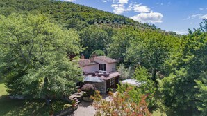 A house surrounded by dense greenery, with a clear sky and a hilly backdrop. - Two-storey villa with large private pool and beautiful landscaped garden (Castiglion Fiorentino)