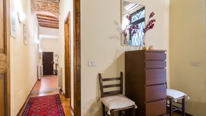 A hallway with a red patterned rug, wooden beams, a radiator, and a chair with a cushion.