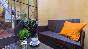 A wicker sofa with an orange cushion, a glass table with a cup and saucer, and a potted plant.