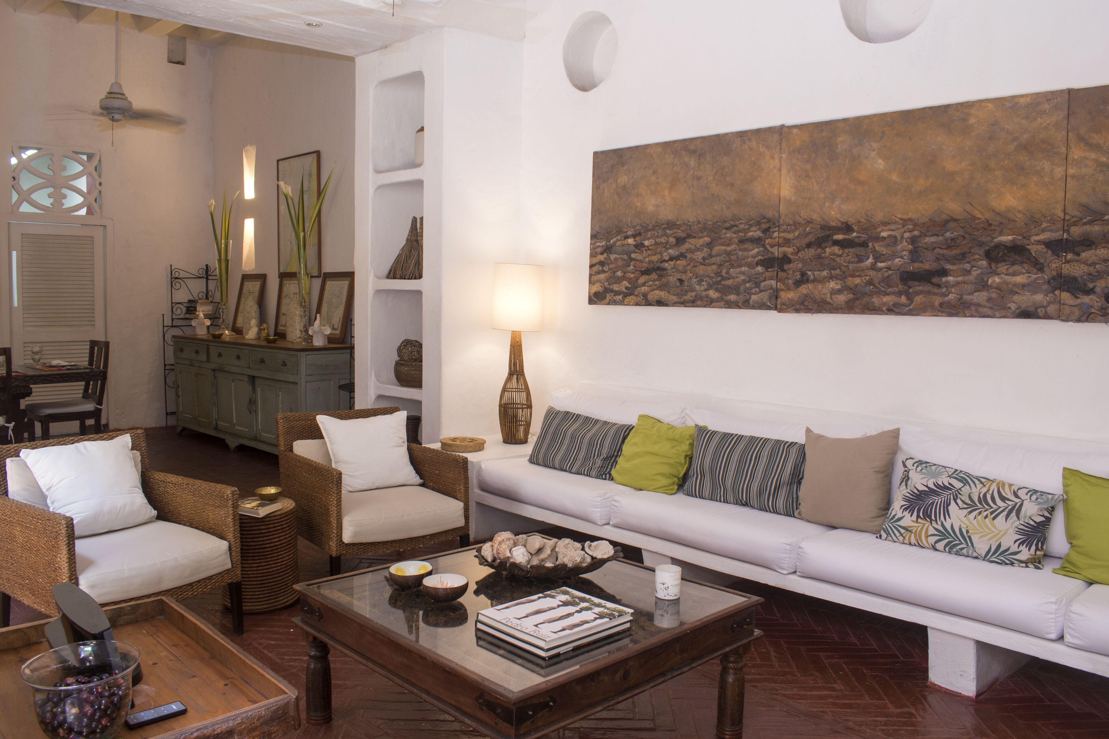 Un salon avec un canapé blanc, des fauteuils en osier, une table basse et un tableau accroché au mur.